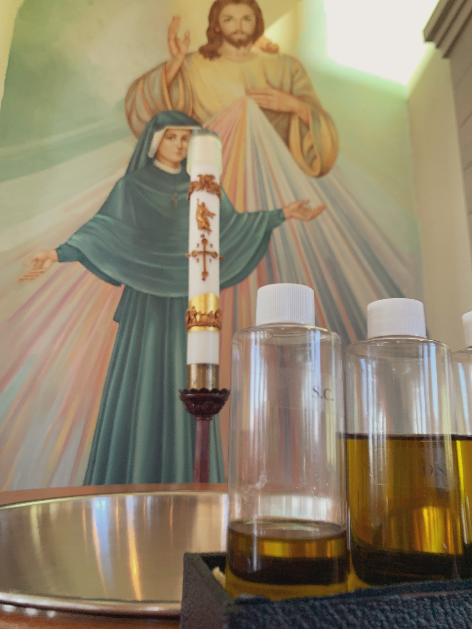 Holy oils on baptismal font with baptismal candle behind