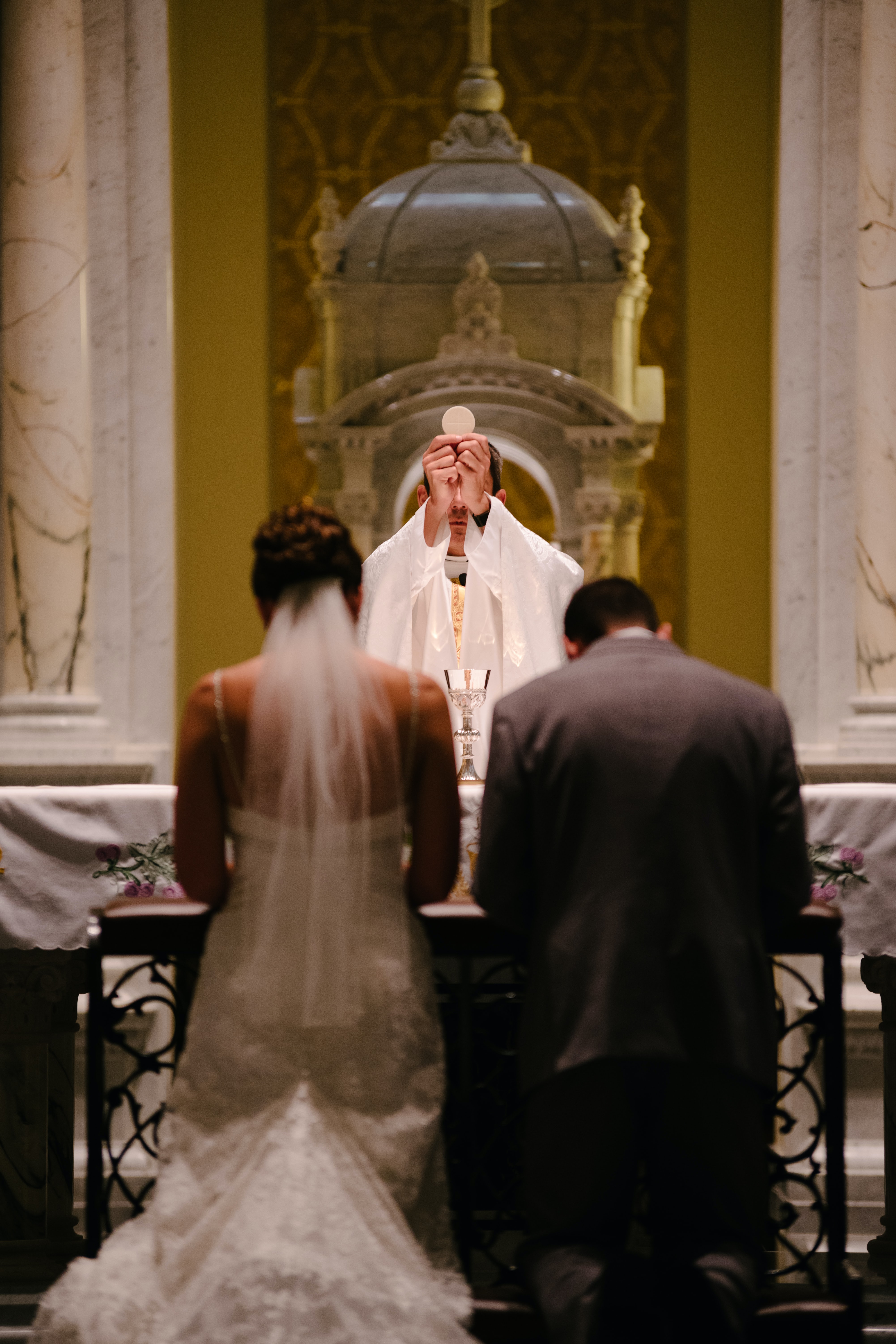 Bride and groom kneeling in front of altar with Priest holding up the Eucharist