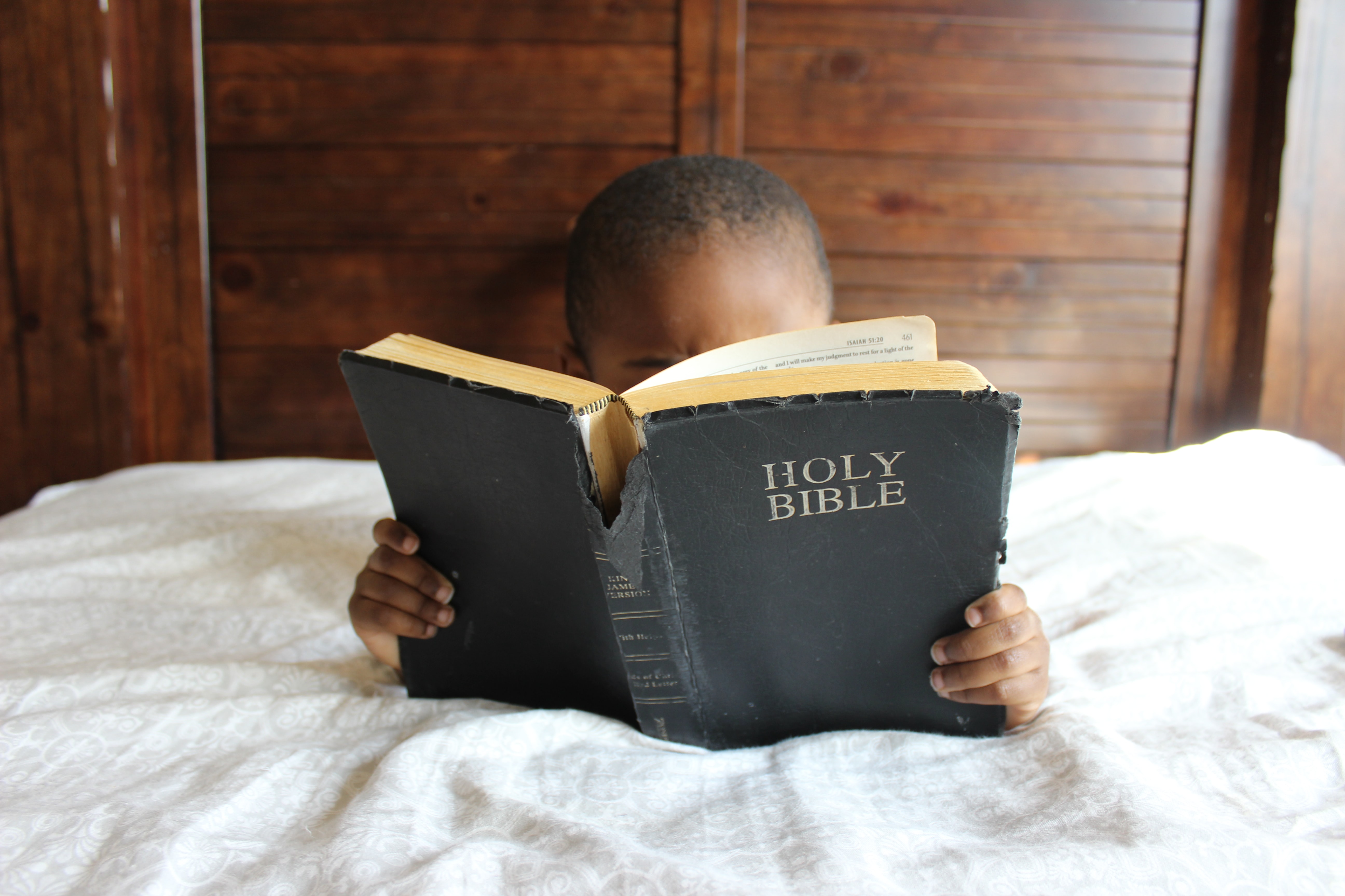 Cute little boy reading a large Bible covering most of his face