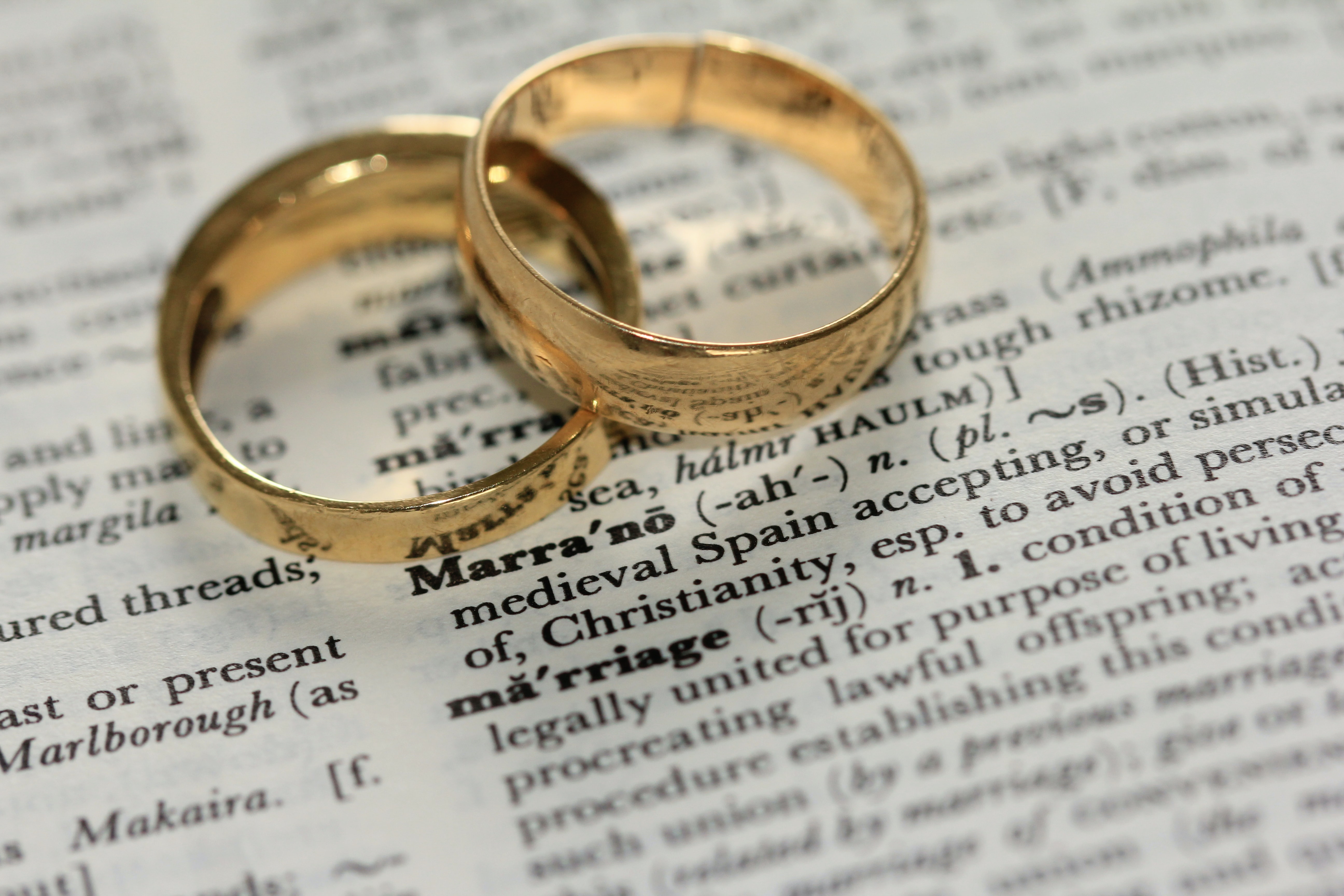 Two gold rings sitting on top of dictionary page with the definition of marriage