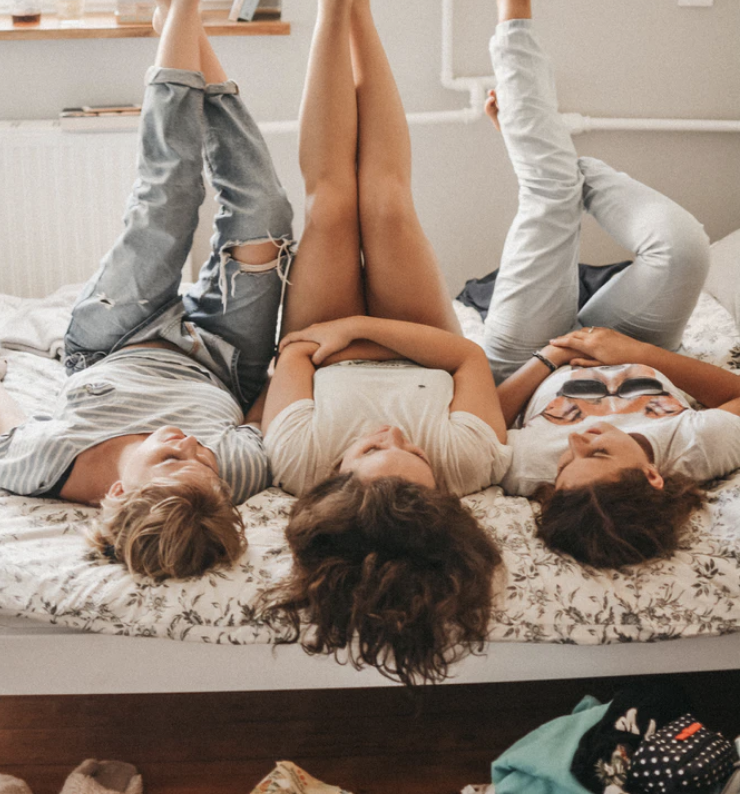 Three girls lying on bed chatting with feet in the air